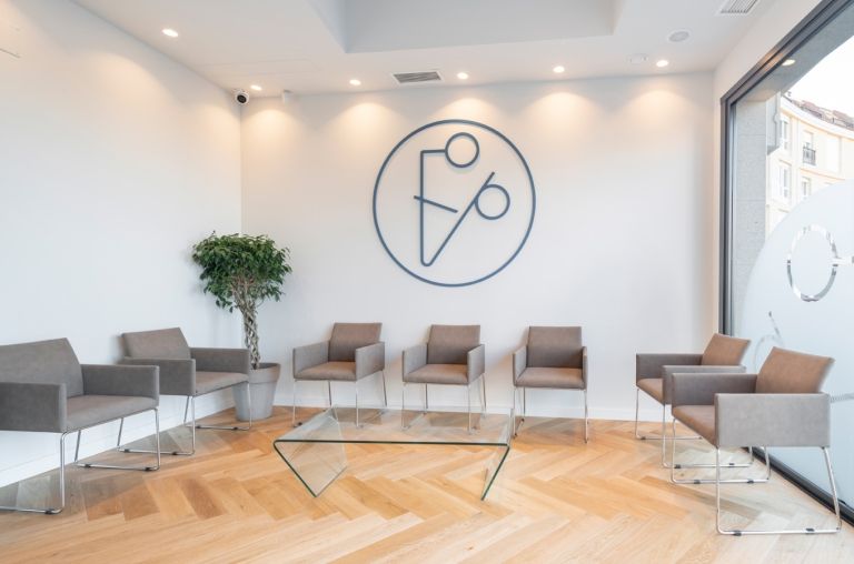 Sala de espera blanca con sillas marrones y logo en pared frontal